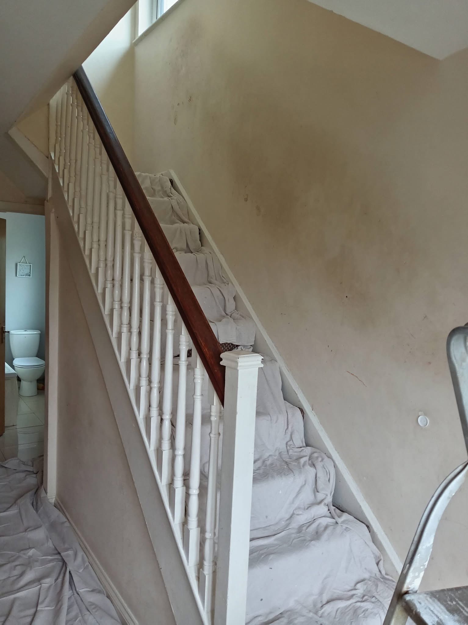 Hallway staircase before painting — bare plaster walls and dust sheets